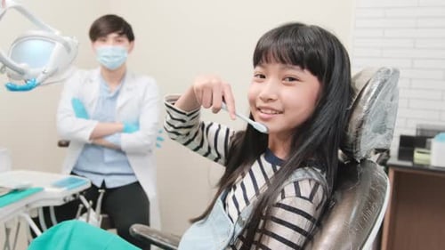 Portrait of an Asian girl with a male pediatric dentist in dental clinic.