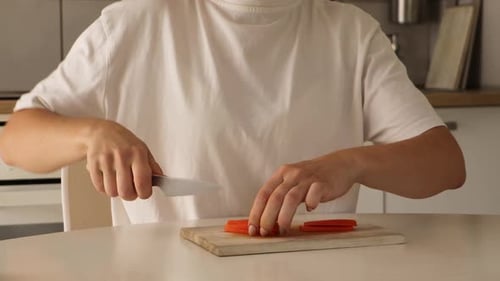 Woman Cuts Carrot on Wooden Board in Kitchen