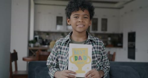 Smiling Boy Holds Father's Day Card at Home