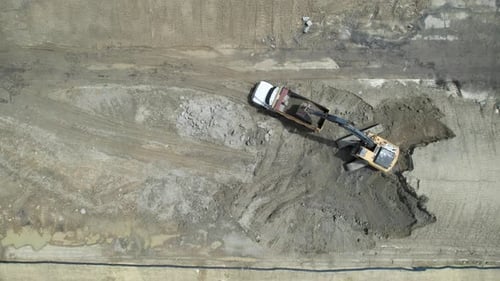 Aerial view of a tractor filling a dumper truck with soil at construction site, project in progress.