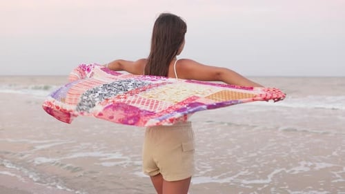 A Girl in a Summer Tshirt and Shorts is Walking Along the Beach Looking at the Horizon and Holding a