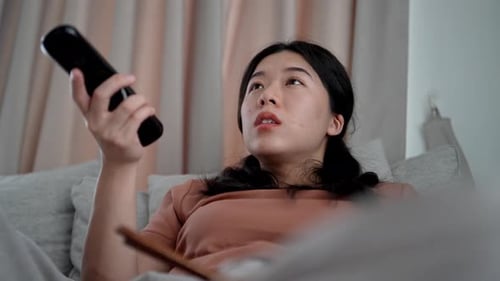 Asian woman sitting on couch and watching television