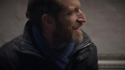 A Man Wearing a Dark Jacket and Scarf Appears Content and Warm in a City Setting During Winter