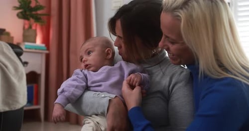 Two women hold infant lovingly inside home
