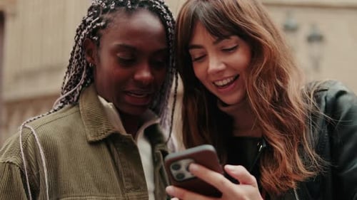Close up of happy women using a smartphone standing outdoors and laughing