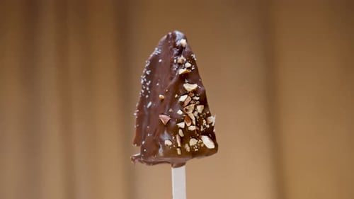 Chocolate cake in the form of Ice cream on a stick, sprinkled with almonds, rotates close-up.