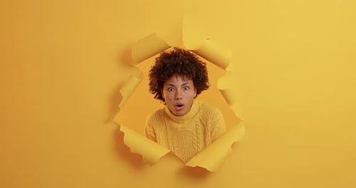 Woman Pops Through Ripped Yellow Paper Smiling Wide