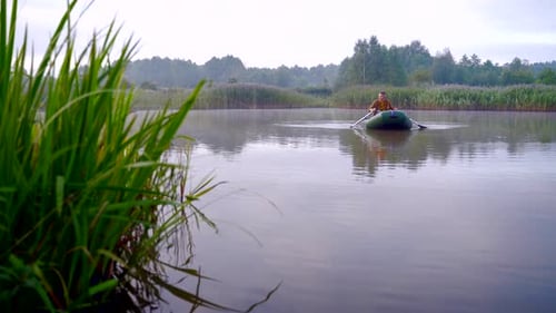young stylish hipster fisherman sails in a boat on a lake or river between the reeds. A young man