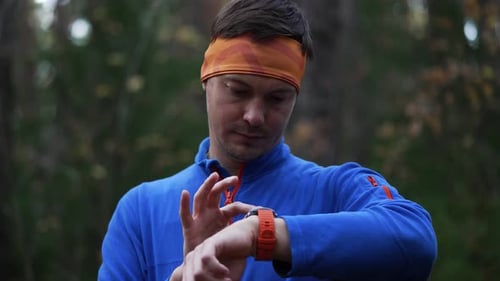 Fit Young Man Checks His Smartwatch After a Run in an Autumn Forest Smiling and Giving an Ok Gesture