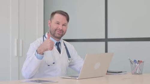 Doctor working on laptop, giving thumbs up in office
