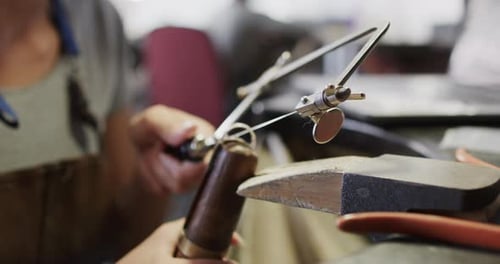 Biracial female worker shaping jewellery with saw in workshop in slow motion