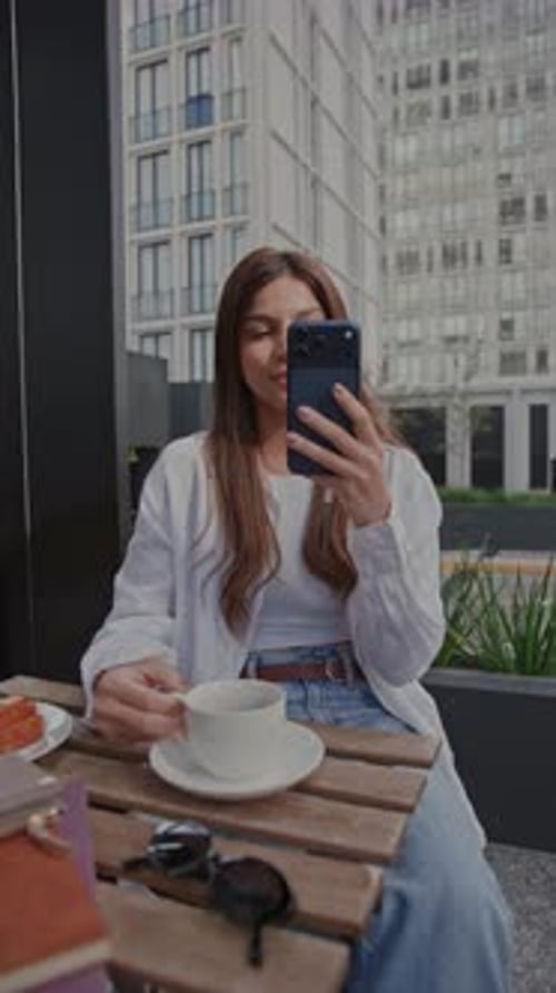 Young Woman Taking a Selfie and Enjoying Coffee at a Sidewalk Cafe