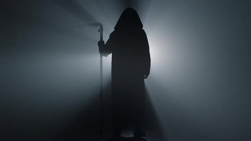 Spooky silhouette of grim reaper with scythe standing in spotlight on halloween