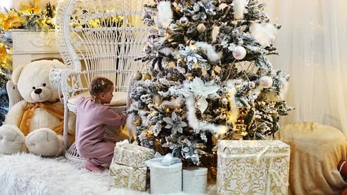 Little Girl Decorates a Snowy Christmas Tree Indoors