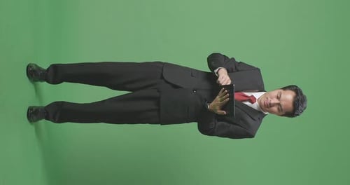 Ganzer Körper eines asiatischen Geschäftsmannes, der lächelt, während er ein Tablet auf Greenscreen-Hintergrund im Studio benutzt