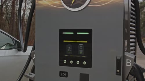 Close up of a electric vehicle charging station charging a car in the background