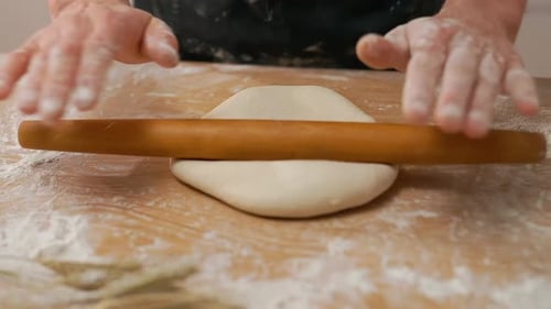 Hands Rolling Dough with Rolling Pin on Table