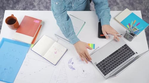 Person at Desk Writing in Notebooks, Using Technology