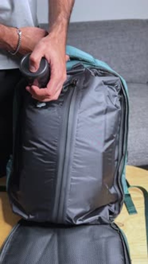 Personne utilisant un aspirateur électrique portable pour comprimer l'air dans un sac à dos de voyage bleu