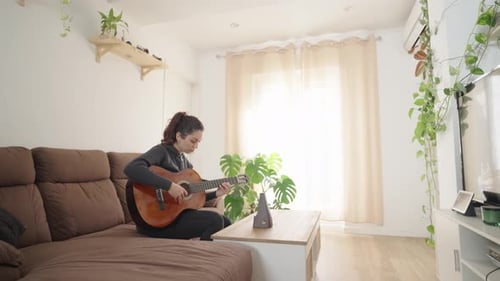 Woman Playing Guitar on Couch at Home