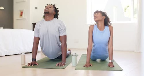 Pareja afroamericana que comienza boca abajo levantando el pecho, presionando las palmas de las manos sobre colchonetas con botellas para hacer yoga
