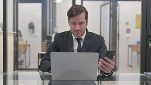 Man Uses Phone and Laptop in Office