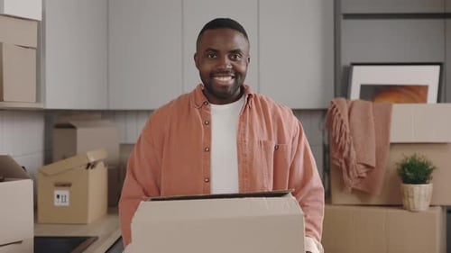 Smiling Young Man Holding a Cardboard Box Indoors
