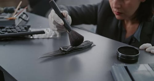 Close Up of Female Forensic Scientist Searching for Fingerprints on Murder Weapon Using Brush