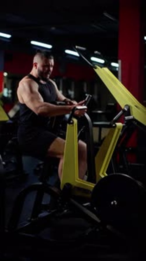 Muscular Man with Focused Expression Using a Rowing Machine in a Dimly Lit Gym