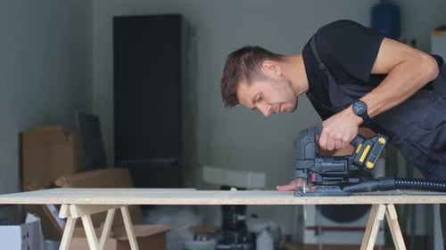 Man Cutting Chipboard with Electric Jigsaw in Home Garage Workshop