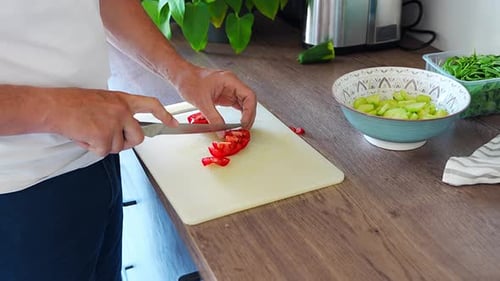 Un homme coupe des tomates rouges pour une salade fraîche dans la cuisine de la maison