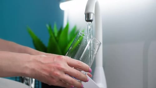 Eco House Young Female Hand with Glass Cup in Hands Pouring Purified Water From Tap in Kitchen Close