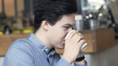 Young teenager happily chatting on cellphone and drinking coffee in cozy cafe