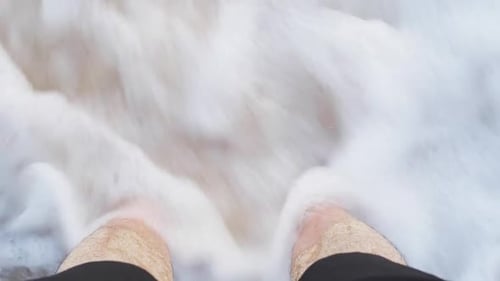 Sea waves washing over male feet, Young Indian man standing on seashore and enjoying tides of sea on