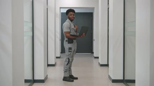 Young Adult Holding Laptop in Modern Office Hallway