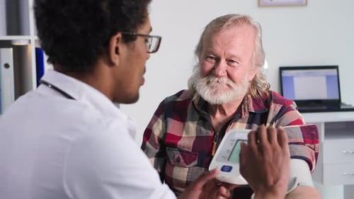 Healthcare an Elderly Man at a Reception at a Young Black Doctor Measures Pressure with Tonometer in
