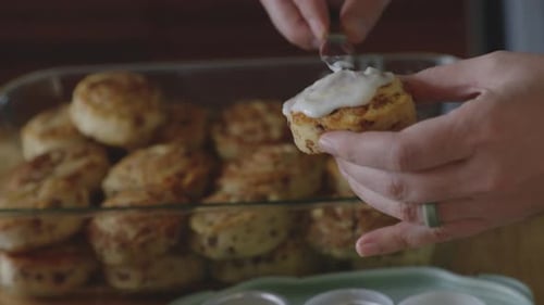 Hands Icing Freshly Baked Cinnamon Rolls