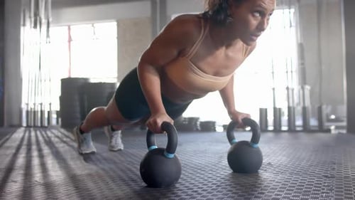 Doing push-ups using kettlebells, woman exercising in gym for fitness