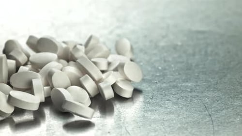White Tablets Spilling Across Textured Metal Filmed on a Highspeed Camera at 1000 Fps
