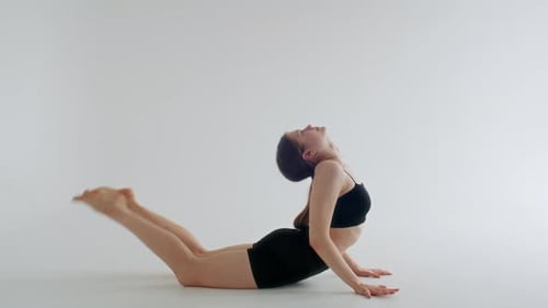 Chica haciendo una postura de yoga doblada hacia atrás con los pies tocando la cabeza en un estudio minimalista