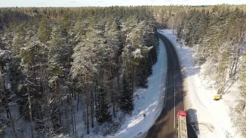 Aerial view of a winding river through a dense snow-covered forest in winter, with a curving road ru