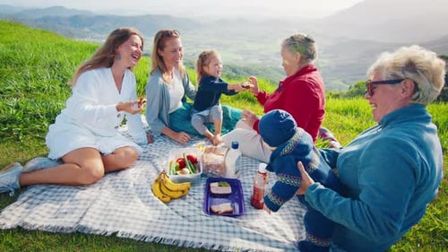 Big Family Have Picnic on the Green Hill in the Mountains at Sunrise
