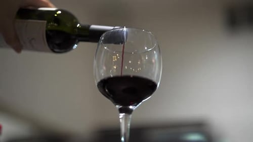 Gros plan du vin rouge versé dans un verre dans une lumière intérieure douce, concentrez-vous sur le flux et le niveau de liquide
