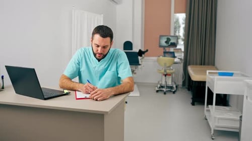 A doctor with a beard conducts an online consultation with a patient using laptop in his office