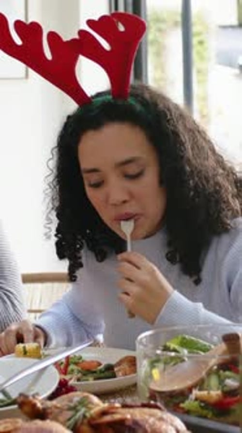 Vertical video: Seeing plate, woman wearing red antlers cutting food with fork at holiday table
