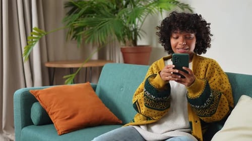 Smiling Woman Using Smartphone on Couch at Home