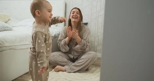 Kleine Tochter tanzt, während die junge Mutter neben ihrer glücklichen Mutter und ihrem Kleinkind in die Hände klatscht