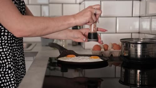 Woman Seasoning Eggs Frying in Pan in Kitchen