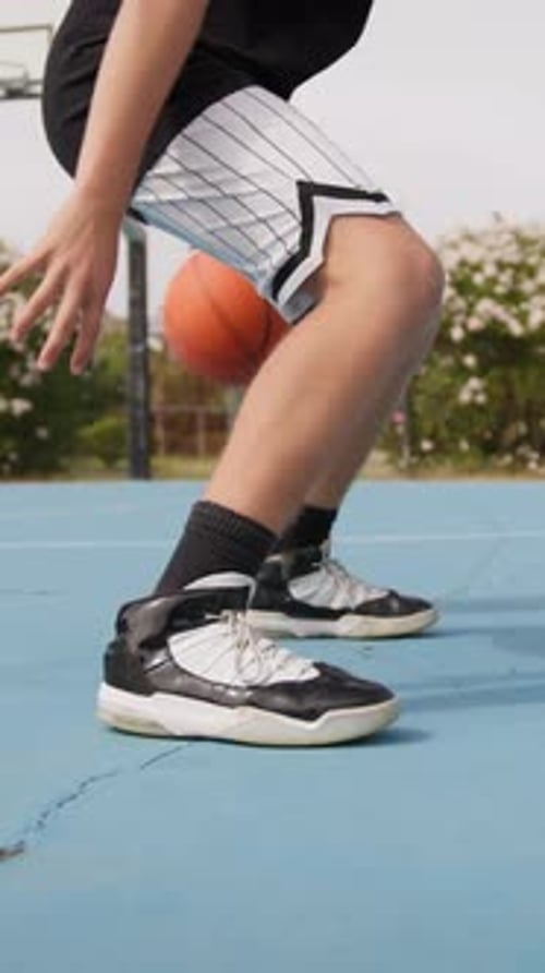 Young Athlete Dribbles With Basketball Under His Legs In Outdoor Field