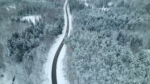 Aerial pan shot showing cars driving on scenic winter road during beautiful snowy day with snow and
